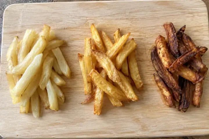 KI-generiertes Symbolbild: Drei Häufchen Pommes auf einem Holzbrett: links zu hell, in der Mitte goldgelb, rechts zu dunkel