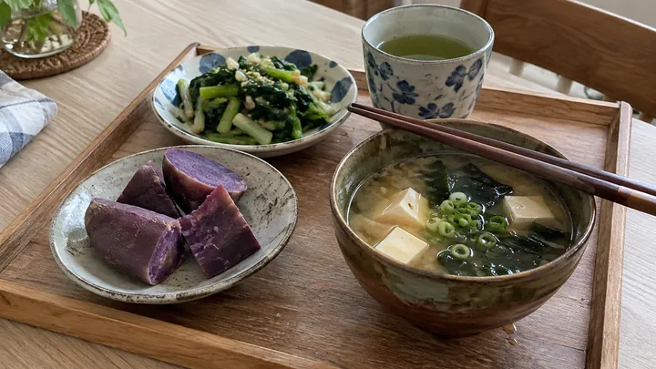 KI-generiertes Symbolbild: Tablett mit einem einfachen Essen nach Okinawa-Art: lila Süßkartoffel, Misosuppe mit Tofu und Algen, gebratenes Grüngemüse und eine Tasse grüner Tee